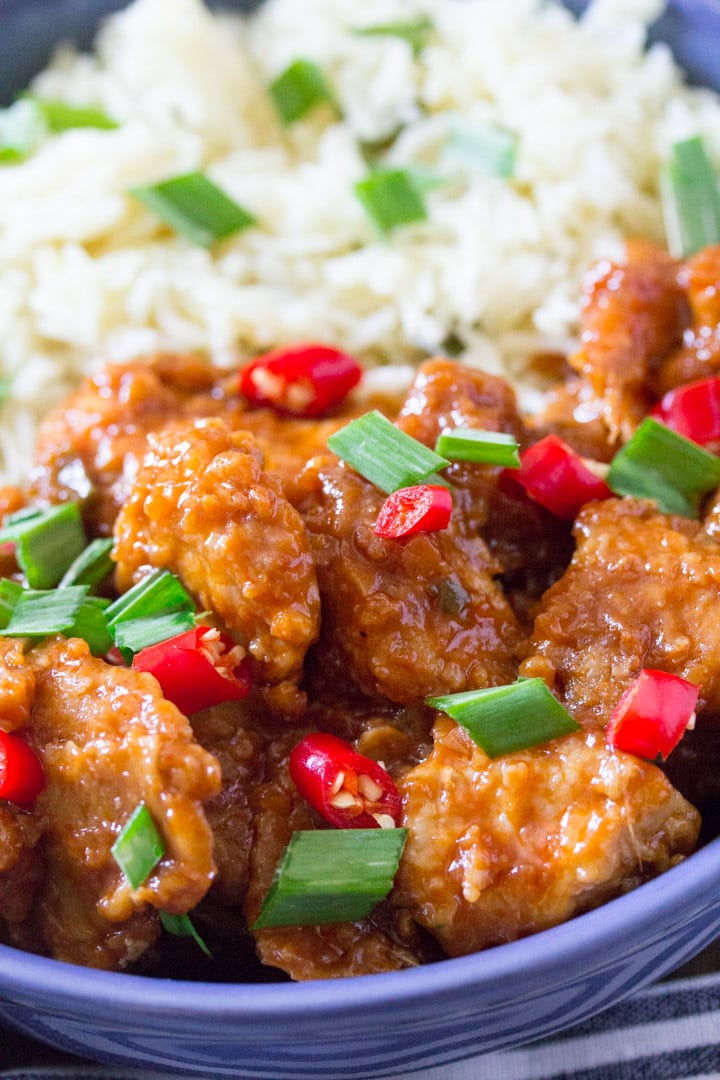 close up 45 degree angle shot of plated chicken manchurian in a blue bowl and garnished with green onions