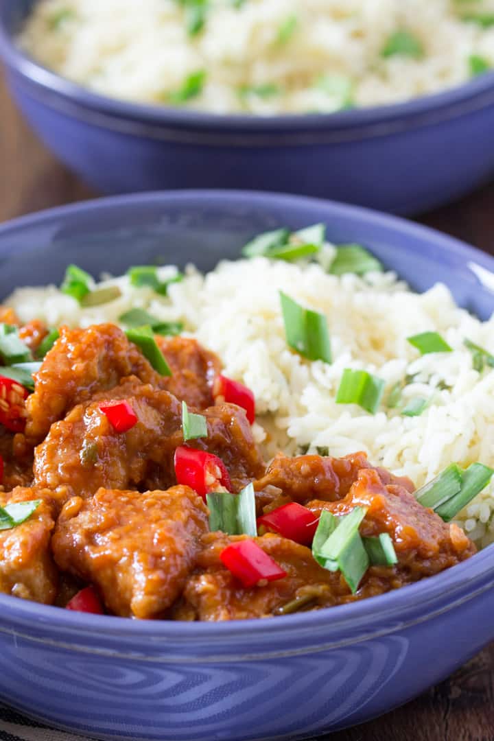 indo-chinese chicken manchurian in a blue bowl with white rice and topped with green onions