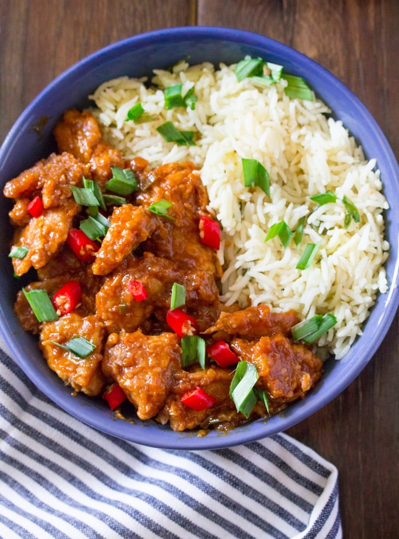 Chicken Manchurian with white rice in a blue bowl and garnished with green onions