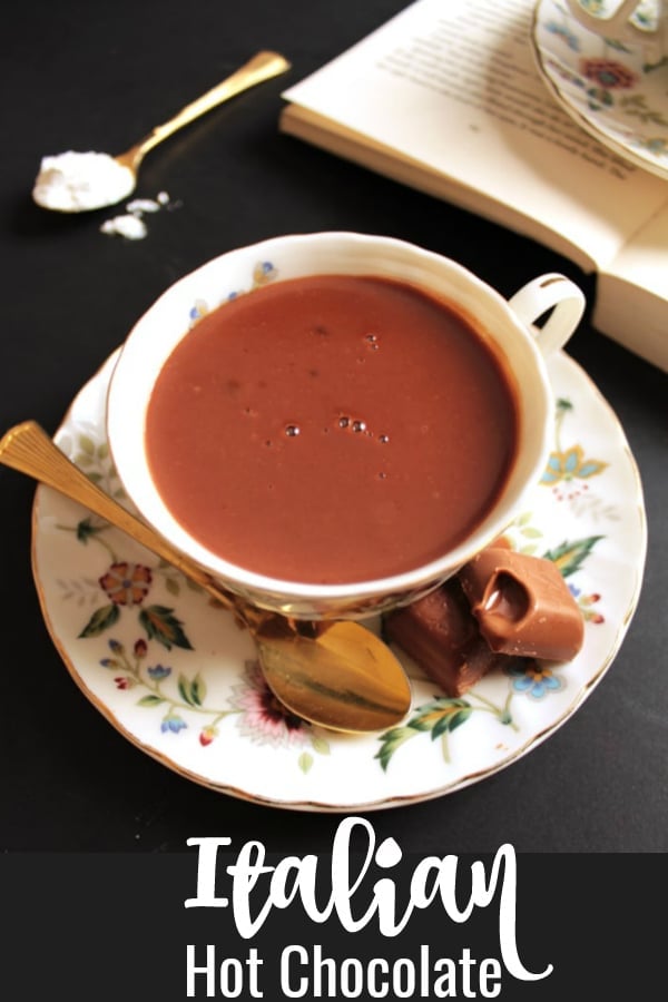 Italian Hot Chocolate in a delicate teacup with a book and some chocolates on the side.