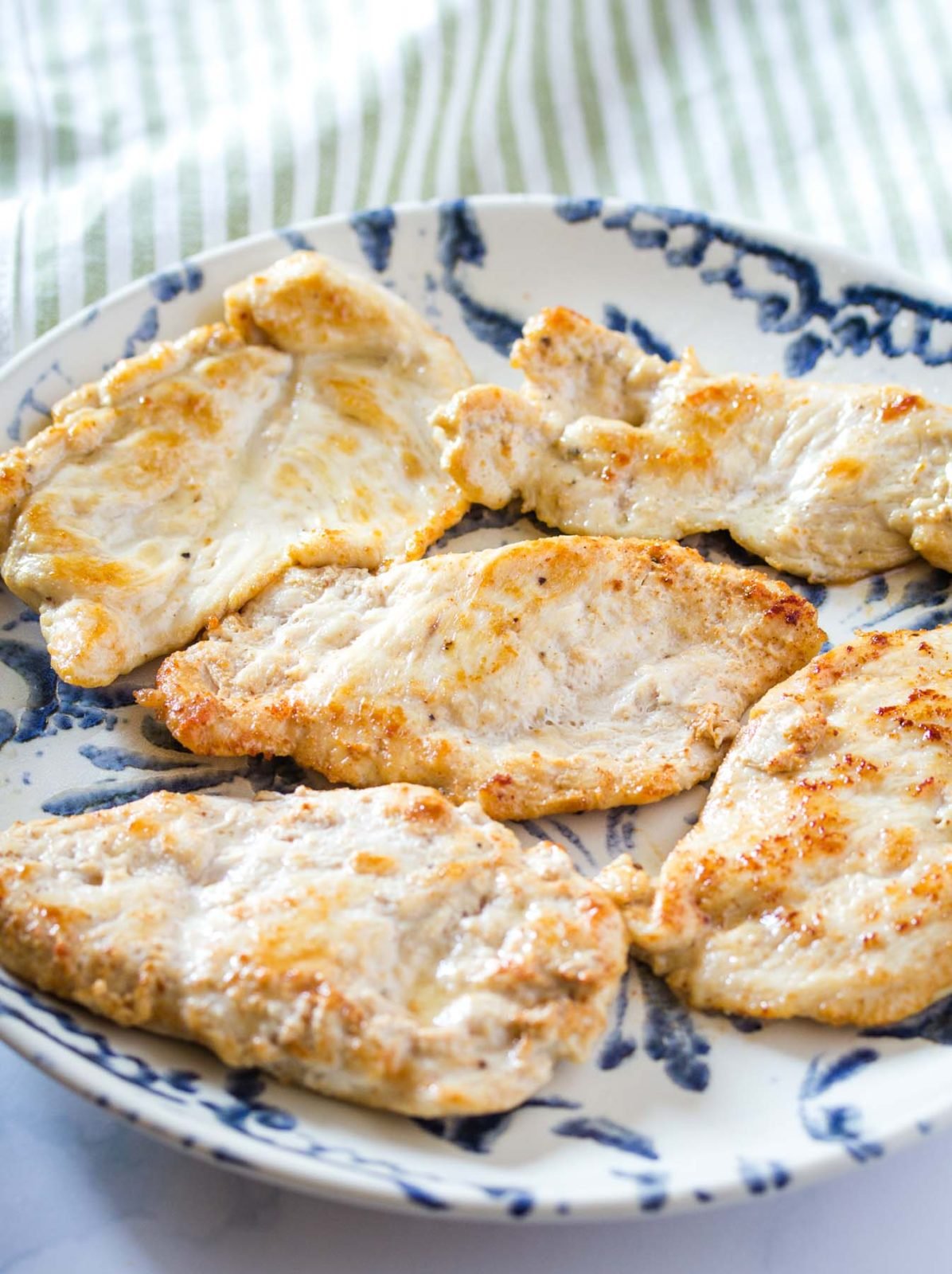 chicken breasts that have been lightly browned and cooked through on a blue and white dinner plate