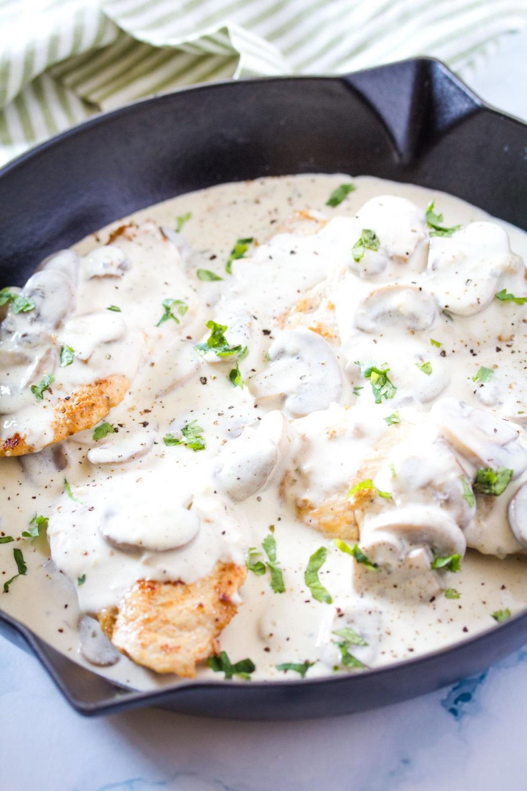 finished creamy mushroom chicken recipe in a cast iron skillet topped with fresh parsley on a sage green and white striped tea towel