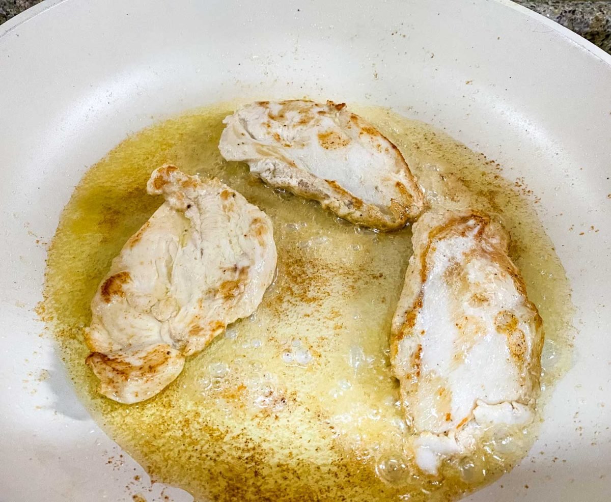 boneless skinless chicken breasts grilling in a pan with butter