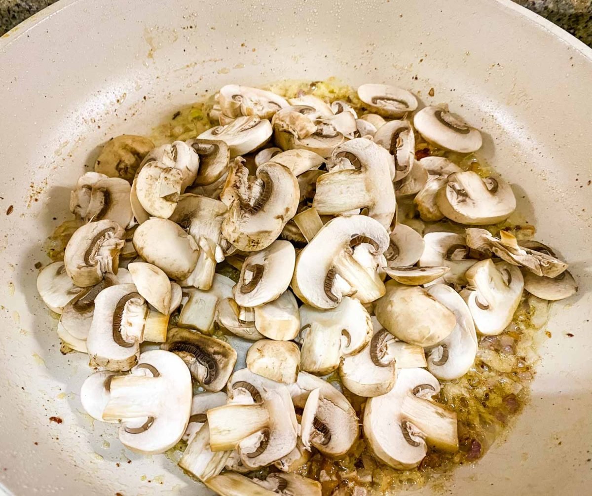 fresh mushroom slices that have been added to sautéed aromatics in a white ceramic pan