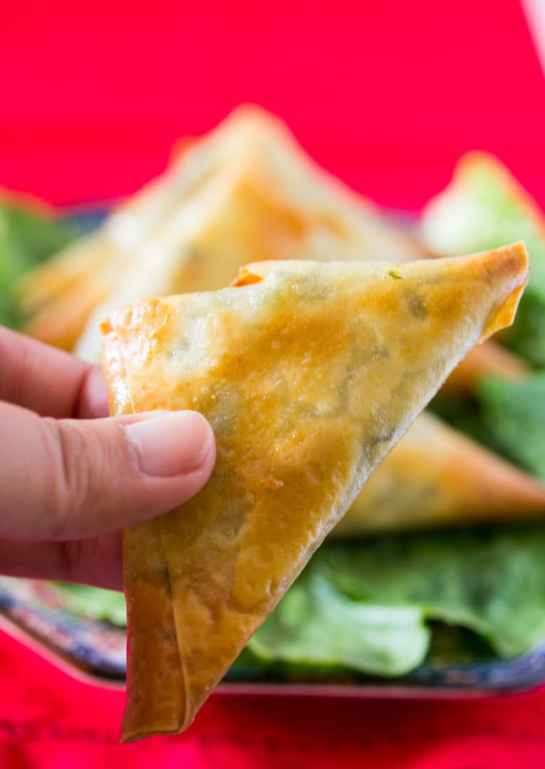 Hand holding baked samosa filled with spinach and feta cheese and cream cheese