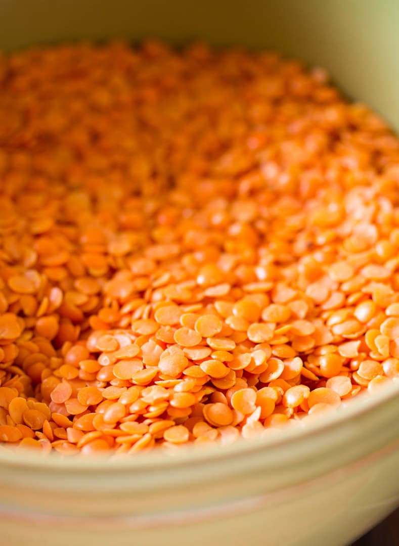 A close up shot split red lentils in a taupe green bowl.