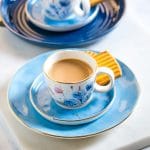 Two small white cups of chai placed on matching blue plates.