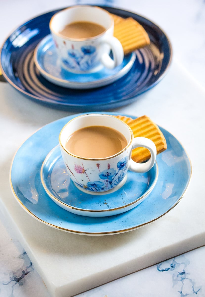 Two small white cups of chai placed on matching blue plates.