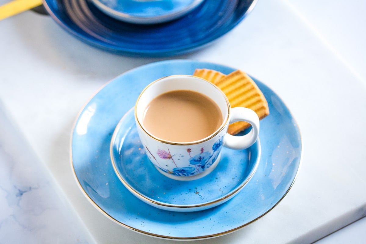 Pakistani milk tea served in a small white tea cup with biscuits.