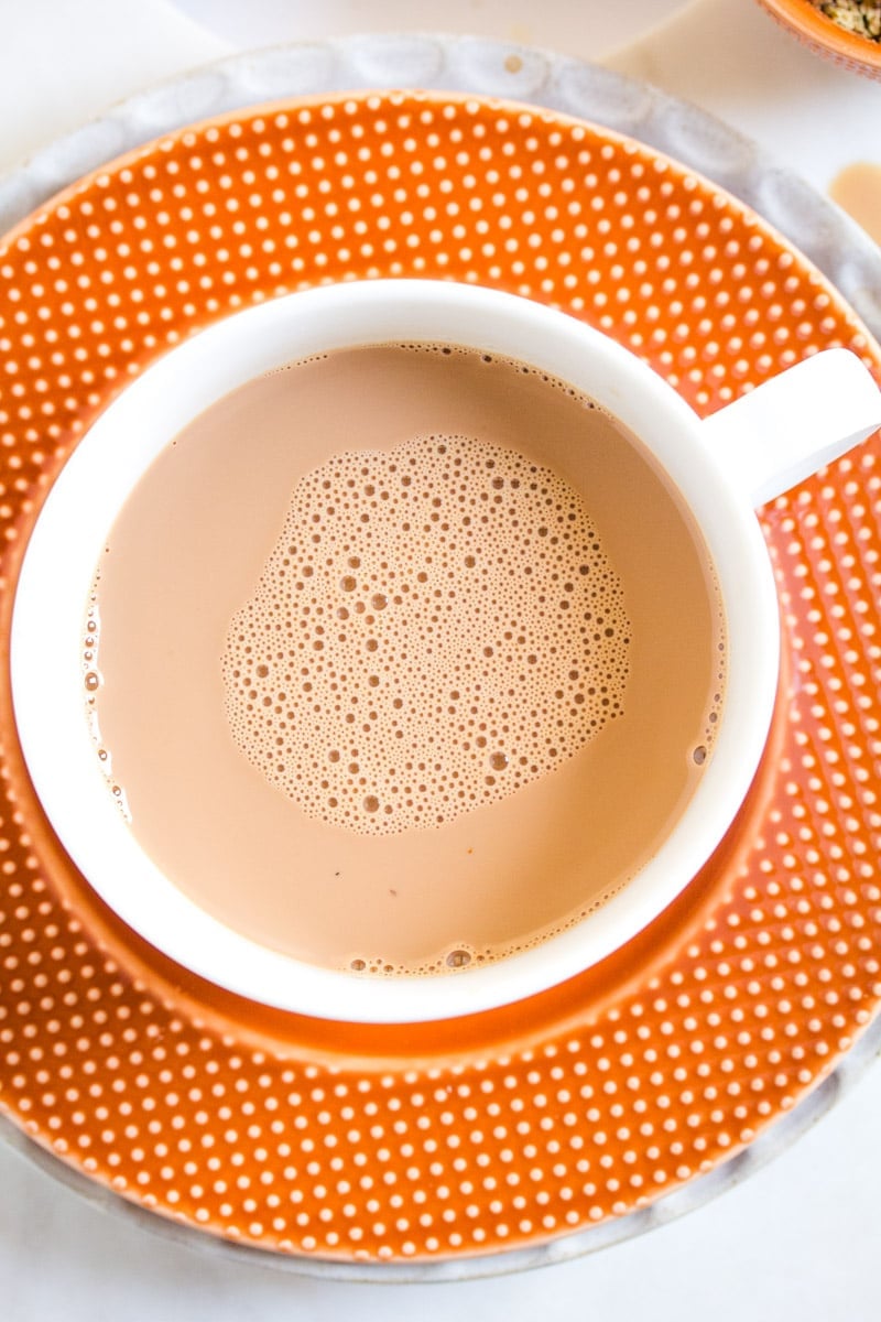 Overhead closeup of masala chai in a white mug on an orange saucer.