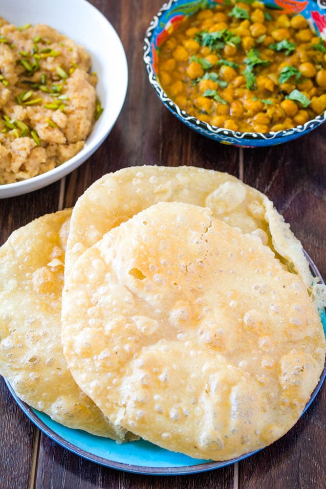 Poori on a blue plate served with chana masala and suji ka halwa