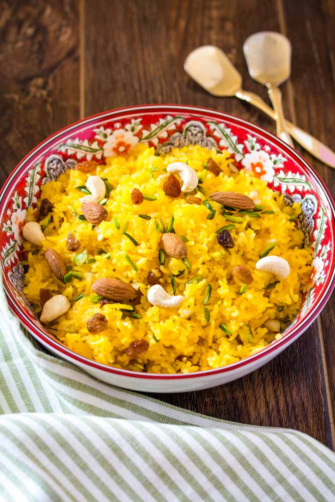 Zarda rice served in a red and white patterend bowl, topped with dry fruit. 