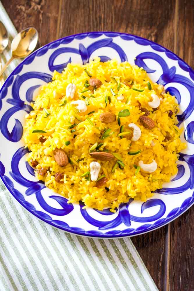 An overhead shot of zarda rice served on a blue and white patterned plate, garnished with dry fruit. 