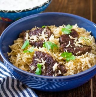 beef yakhni pulao in a blue bowl served with a side of raita