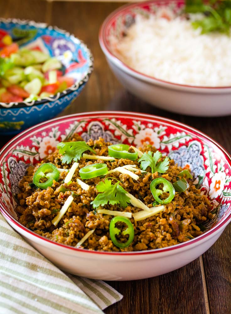 Pakistani beef keema served in a red patterned bowl topped with green chillies, ginger, and coriander. 