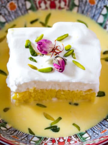 Saffron Milk Cake in a red bowl with rose buds and slivered pistachios