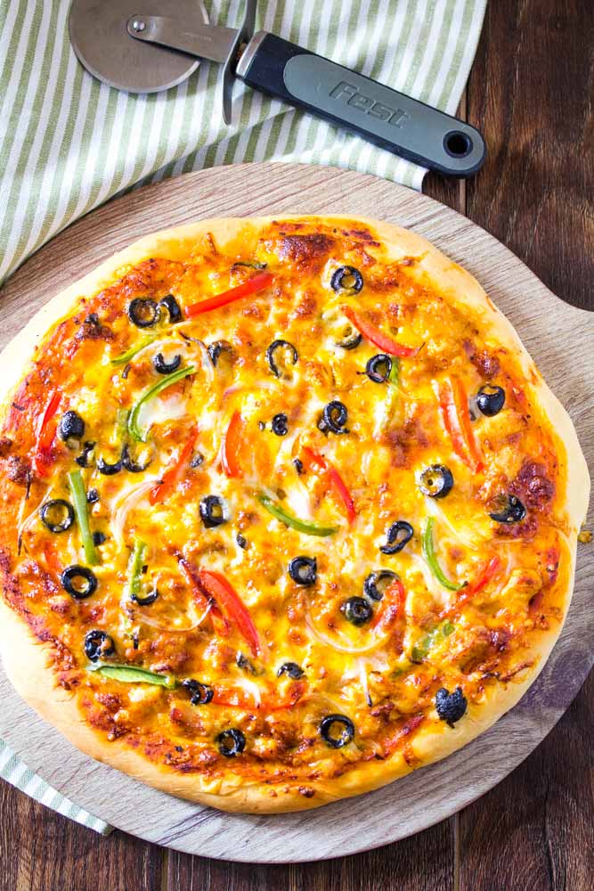 Whole tandoori chicken pizza with pizza cutter nearby.