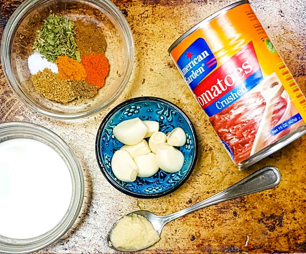 Ingredients for chicken tikka masala: crushed tomatoes, spices, garlic cloves, ginger paste and heavy cream. 