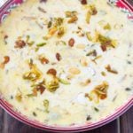 sheer khurma in a red bowl topped with roasted nuts