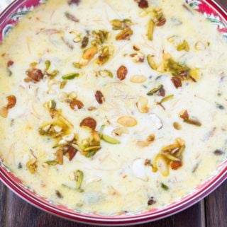 sheer khurma in a red bowl topped with roasted nuts