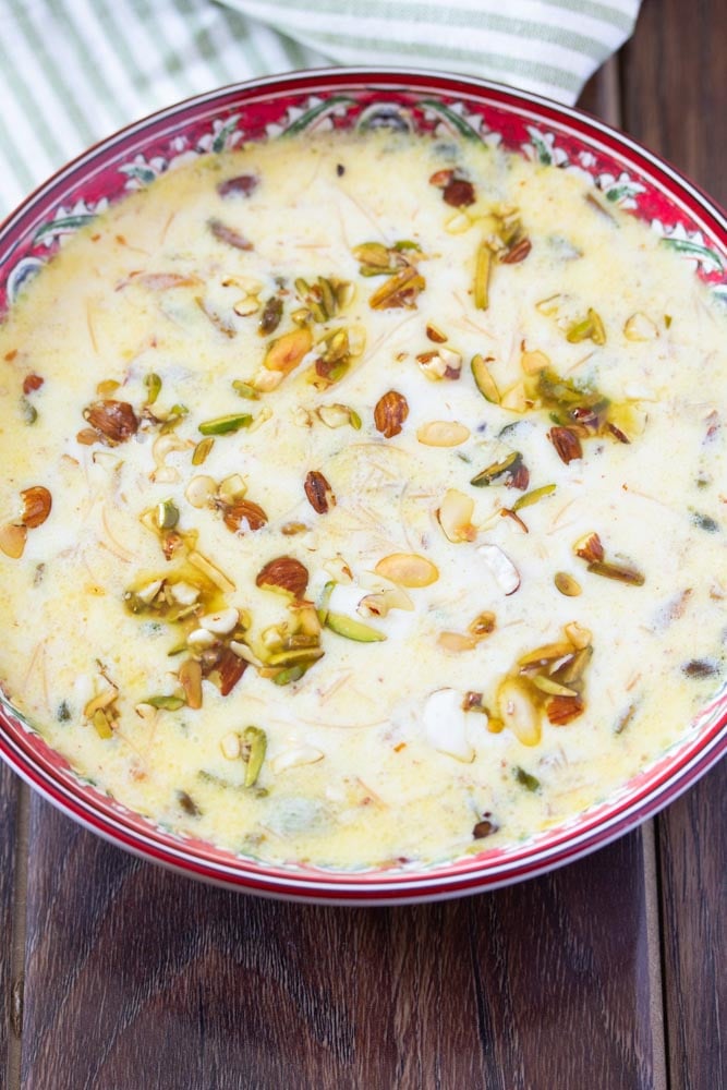 Sheer khurma in a red bowl topped with roasted nuts.