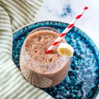 Coffee Banana Smoothie in a round glass with a red and white striped straw.