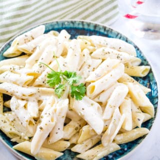 Creamy Garlic Pasta on a blue plate topped with coriander, on white marble backdrop.