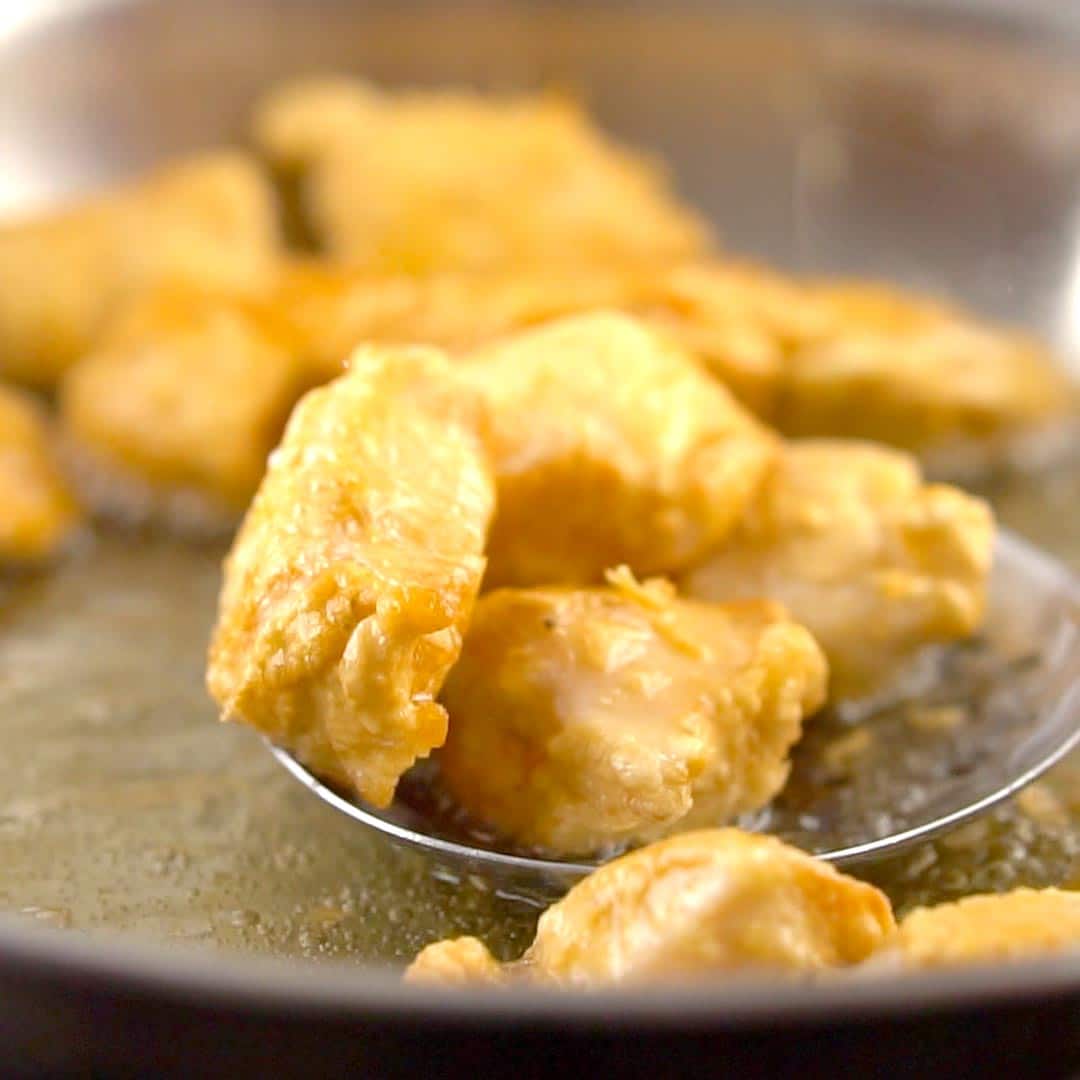 golden pieces of fried chicken being removed from wok with a slotted spoon