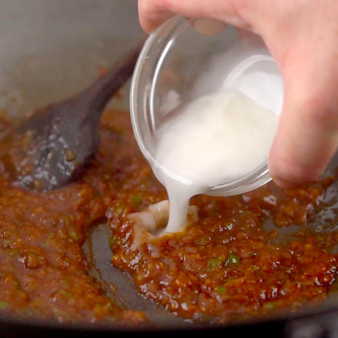 hand pouring in cornstarch slurry to manchurian sauce