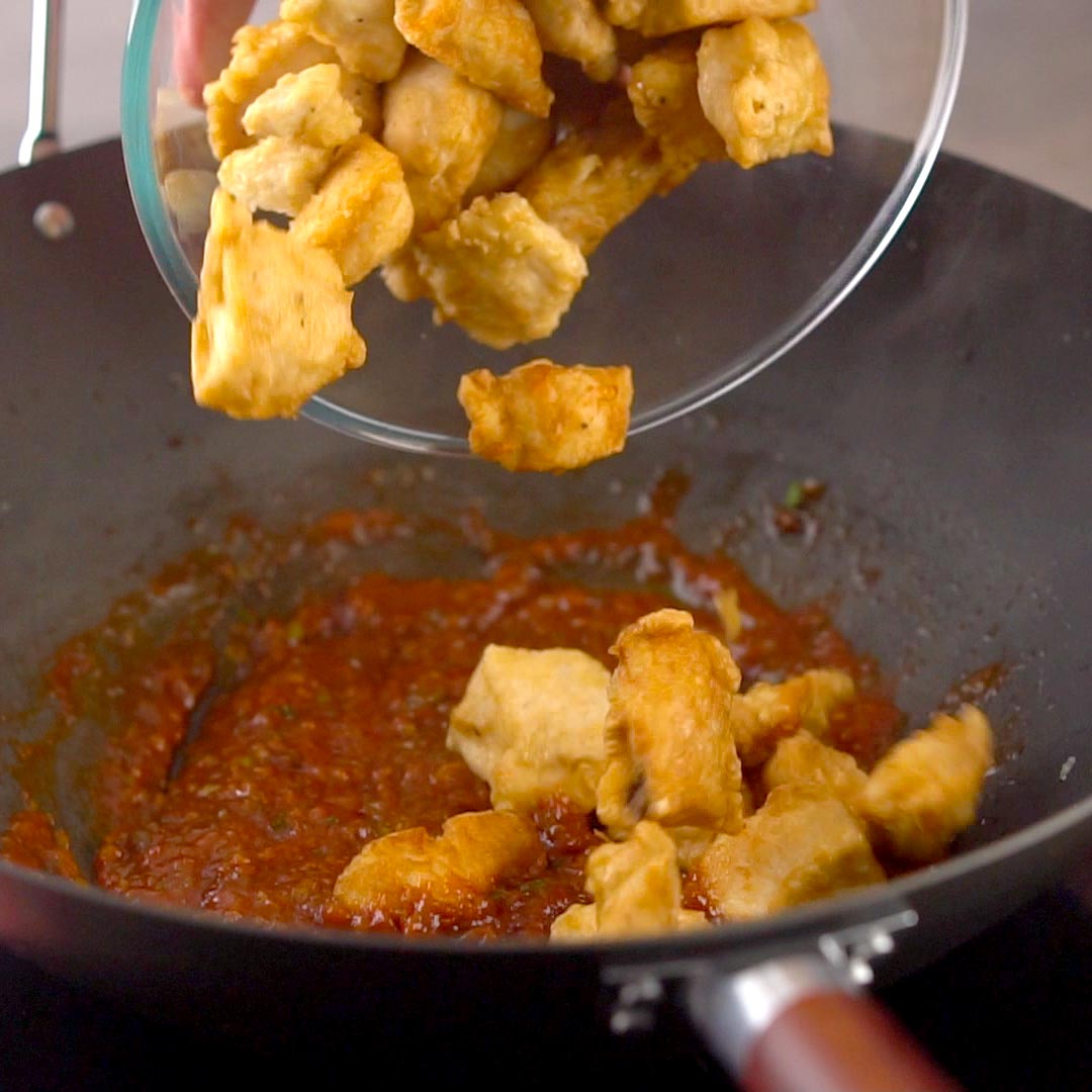 fried chicken nuggets being poured into wok with manchurian sauce