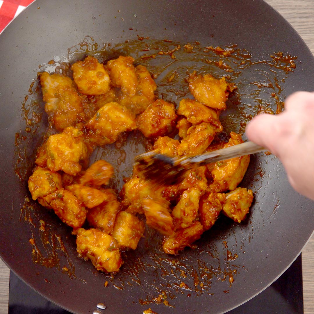 hand stirring together fried chicken pieces and manchurian sauce