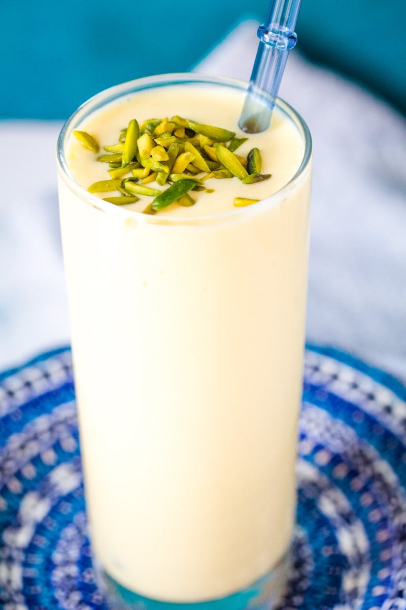 Mango Lassi in a tall glass with a blue straw.