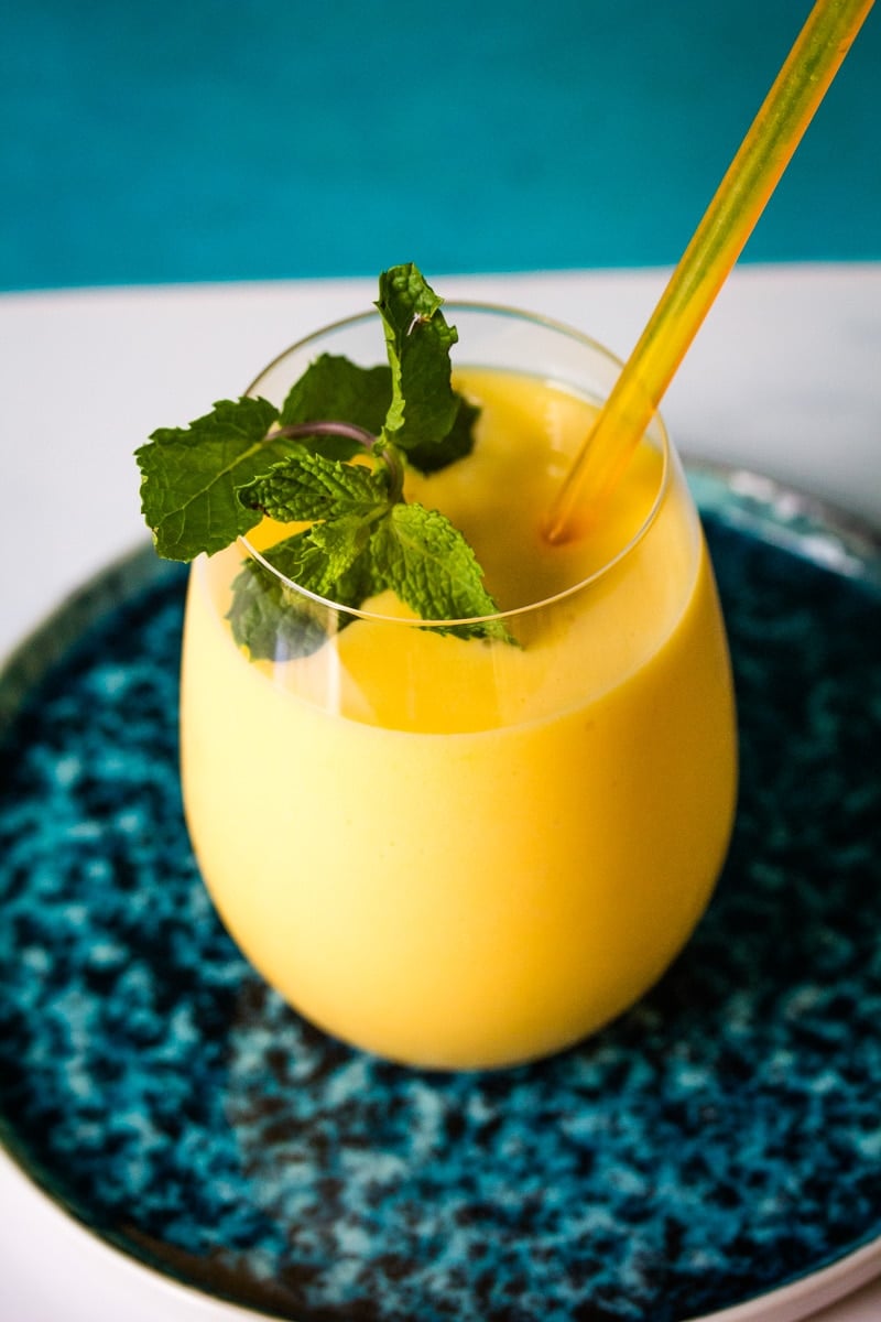 Creamy mango milkshake in a large glass with mint leaves.