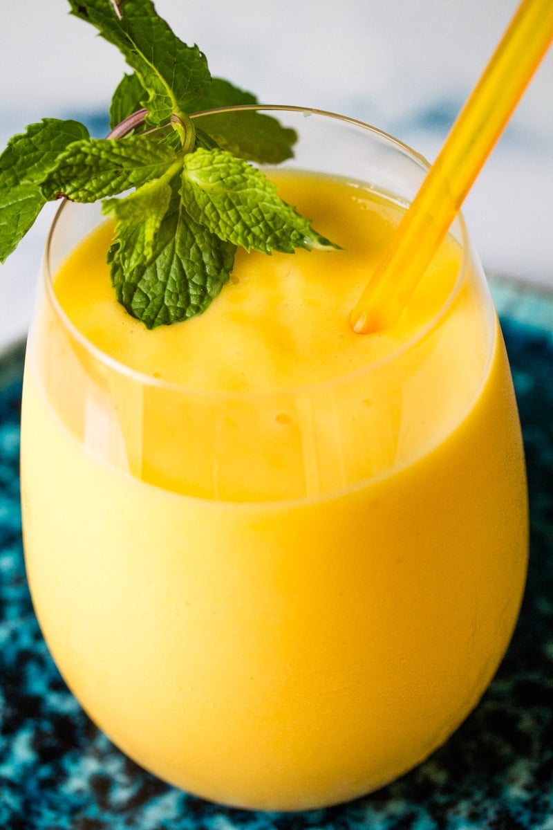 Mango milkshake in a glass with a sprig of mint and a yellow straw.