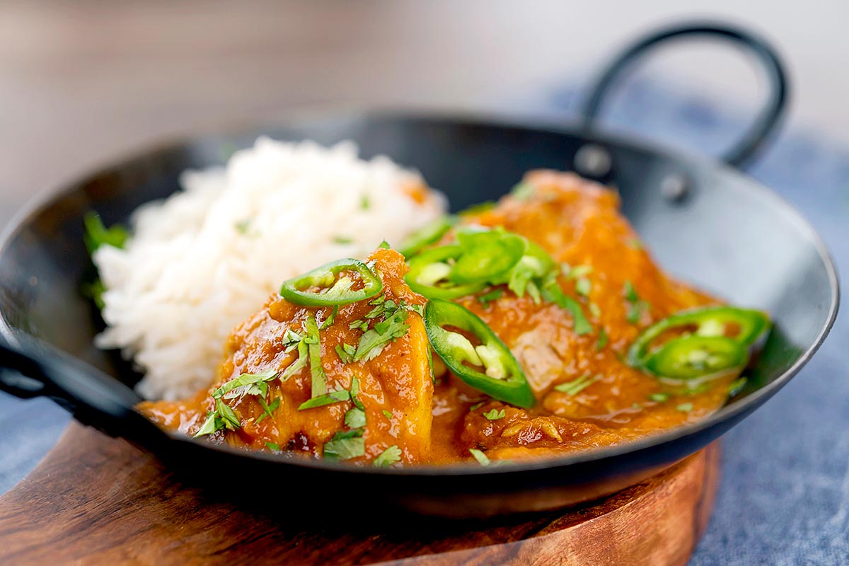 Karahi topped with coriander and green chillies in a black wok.