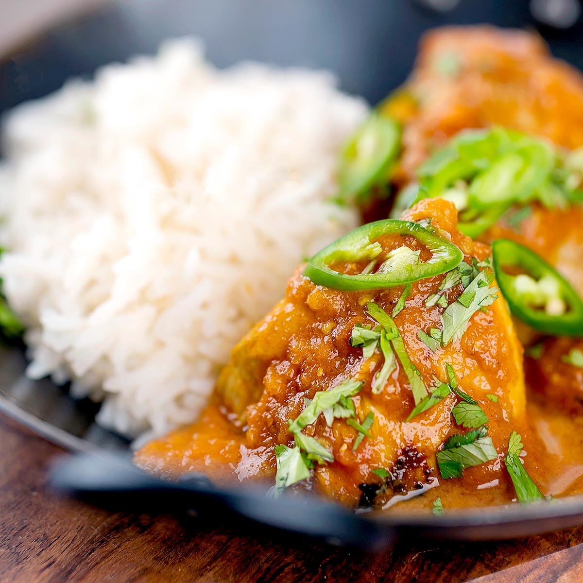 Close up shot of chicken karahi with white rice in a black wok. 