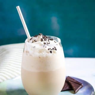 cold coffee with in a glass on a blue plate with a white straw inserted