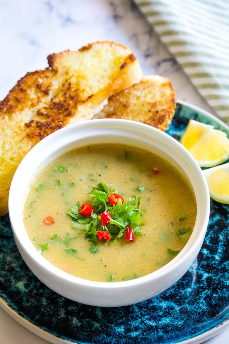 red lentil soup in a white bowl topeed with red chillies and coriander.