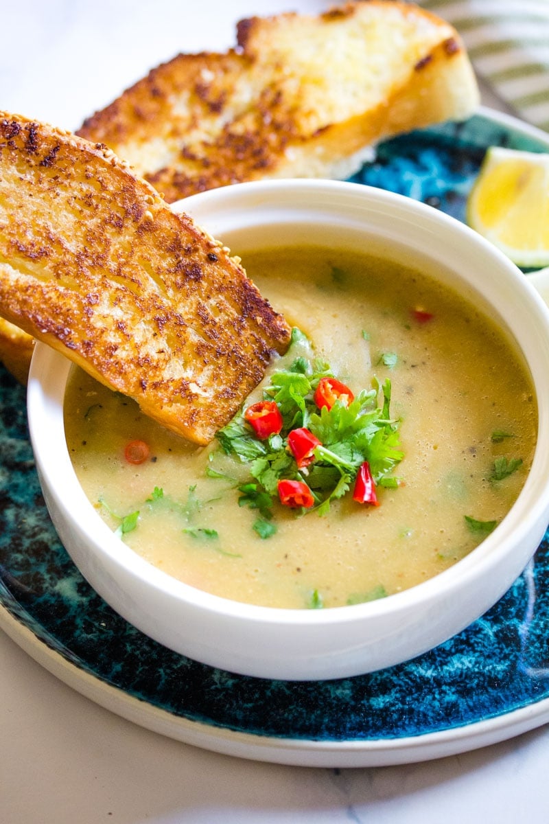 buttered toast dipped into lentil soup in a white bowl.