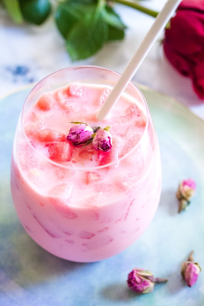 close up of watermelon milkshake in a glass topped with dried rose buds.