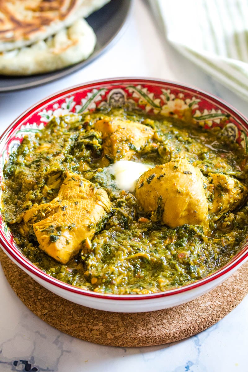 Close up of Pakistani chicken palak in a red bowl placed on top of brown table pad.