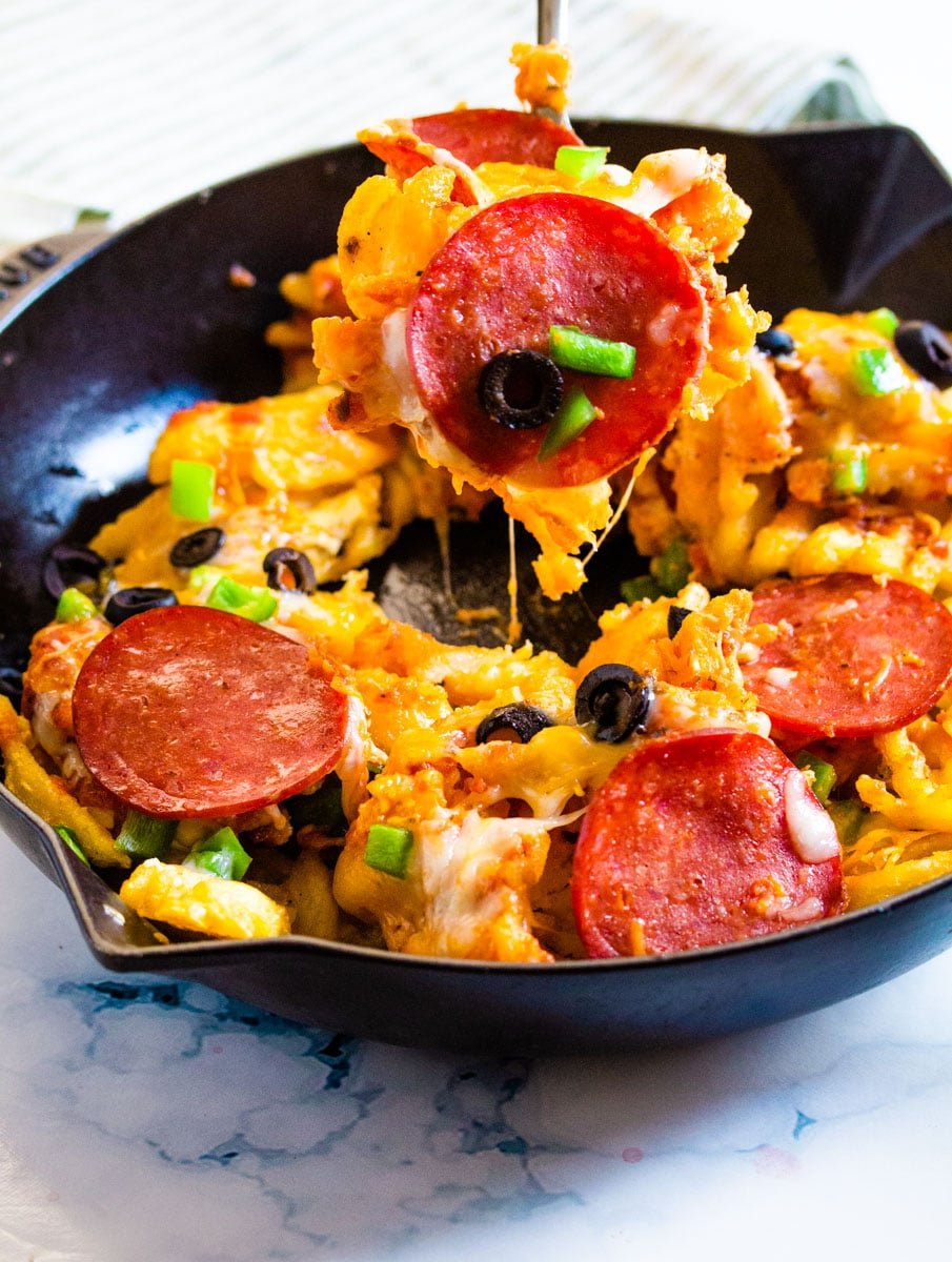 Shot of pizza fries being scooped out of a black cast iron skillet. 