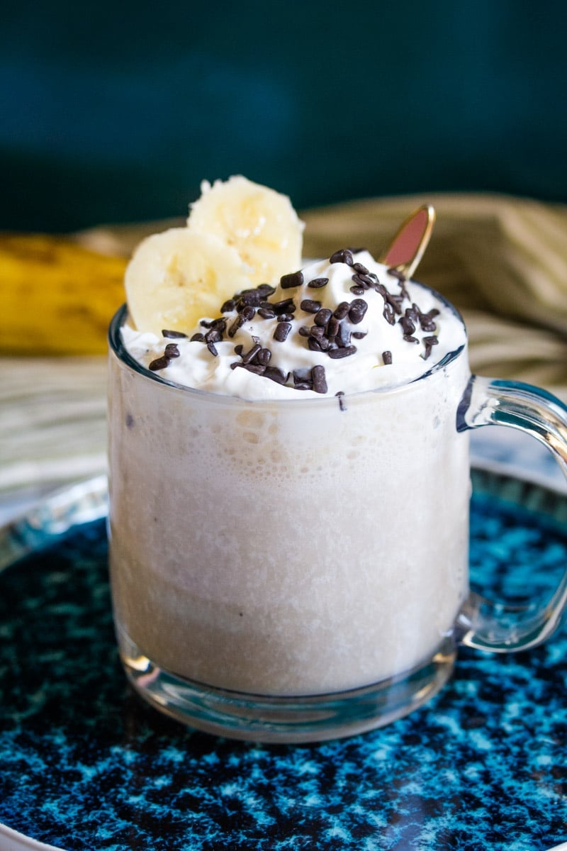 banana milkshake in a glass bug topped with whipped cream, sprinkles and banana slices.