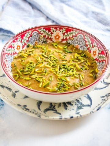 besan halwa in a red patterned bowl, topped with slivered pistachios.