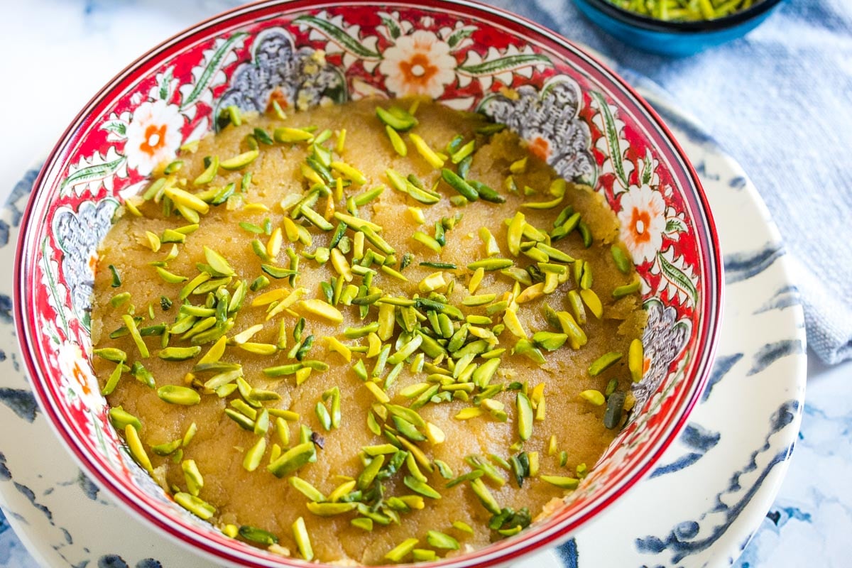 Pakistani dessert made with gram flour and milk, served in a red patterned bowl with a small of bowl of pistachios in the background. 