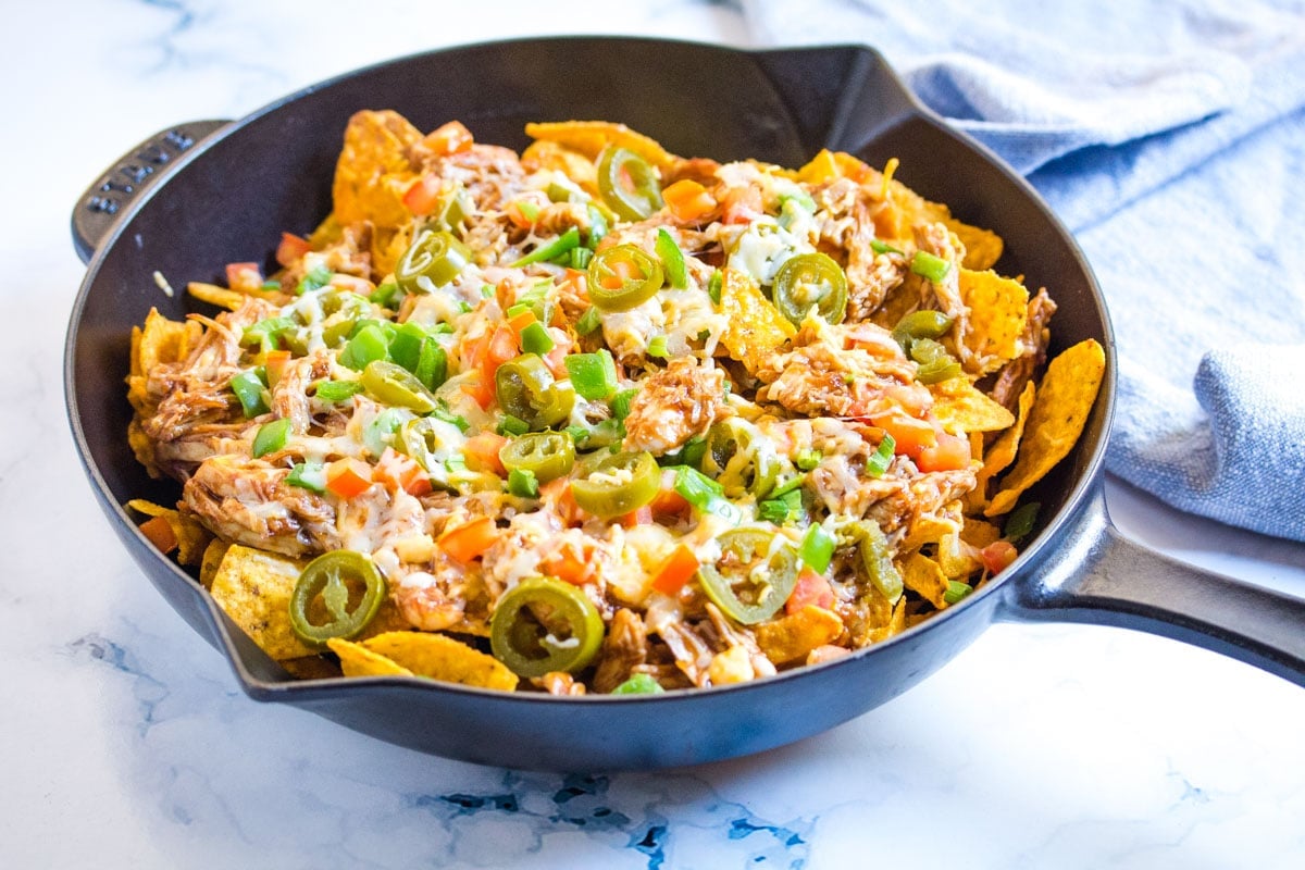 A skillet full of cheesy baked doritos chips topped with saucy bbq chicken.