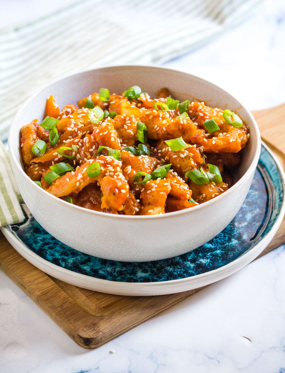 crispy chicken strips coated in a spicy and sweet sauce topped with green onions and sesame seeds. 
