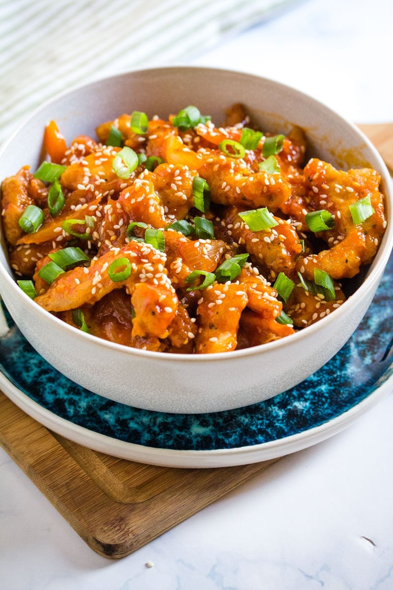 Dragon chicken served in a light grey bowl garnished with green onions and sesame seeds.