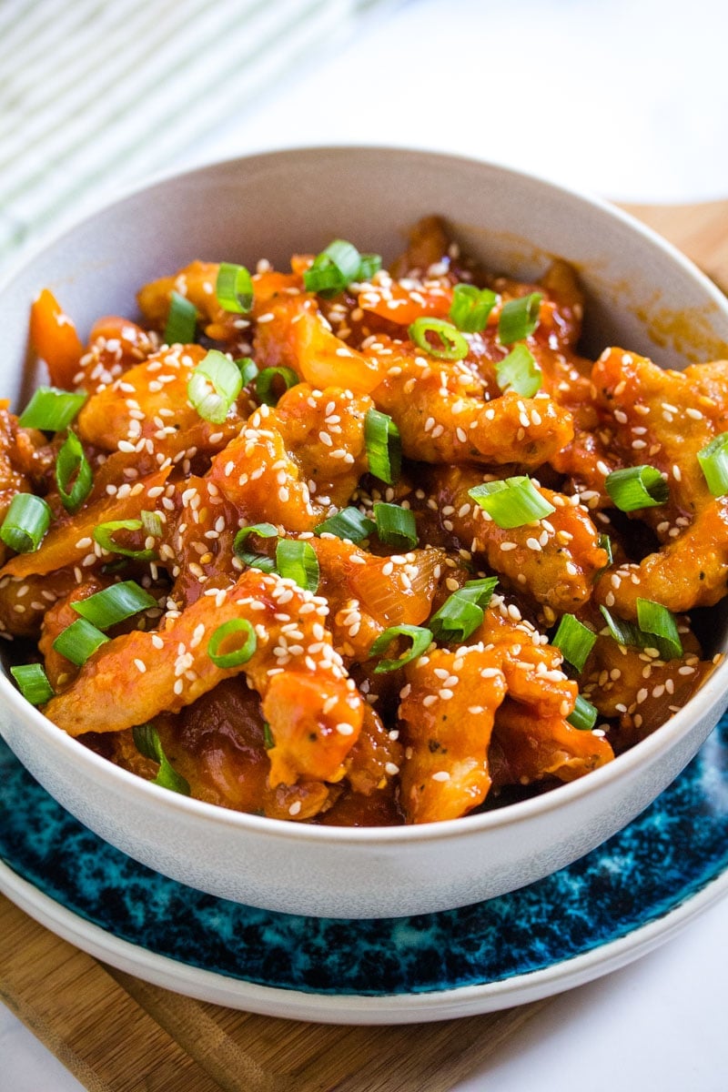 crispy fried chicken dragon coated in a sweet and spicy sauce in a light grey bowl.