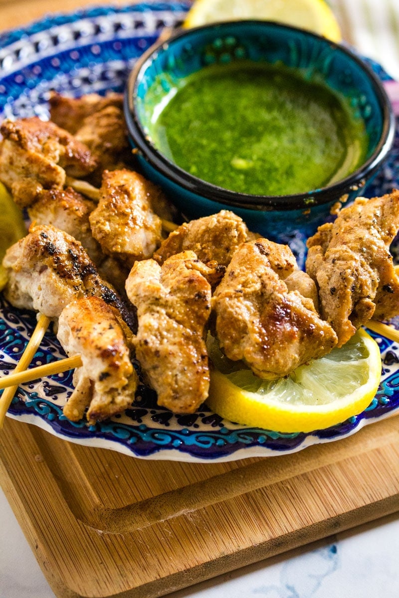 creamy, soft malai tikka boti on a blue plate served with a small bowl of green chutney.